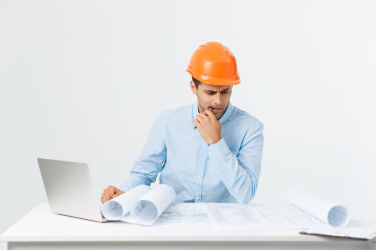 Portrait of confused male designer or architect, feels stressed, being nervous, keeps hand on head, stares in blueprint. Exhausted man creates construction project alone, has some troubles